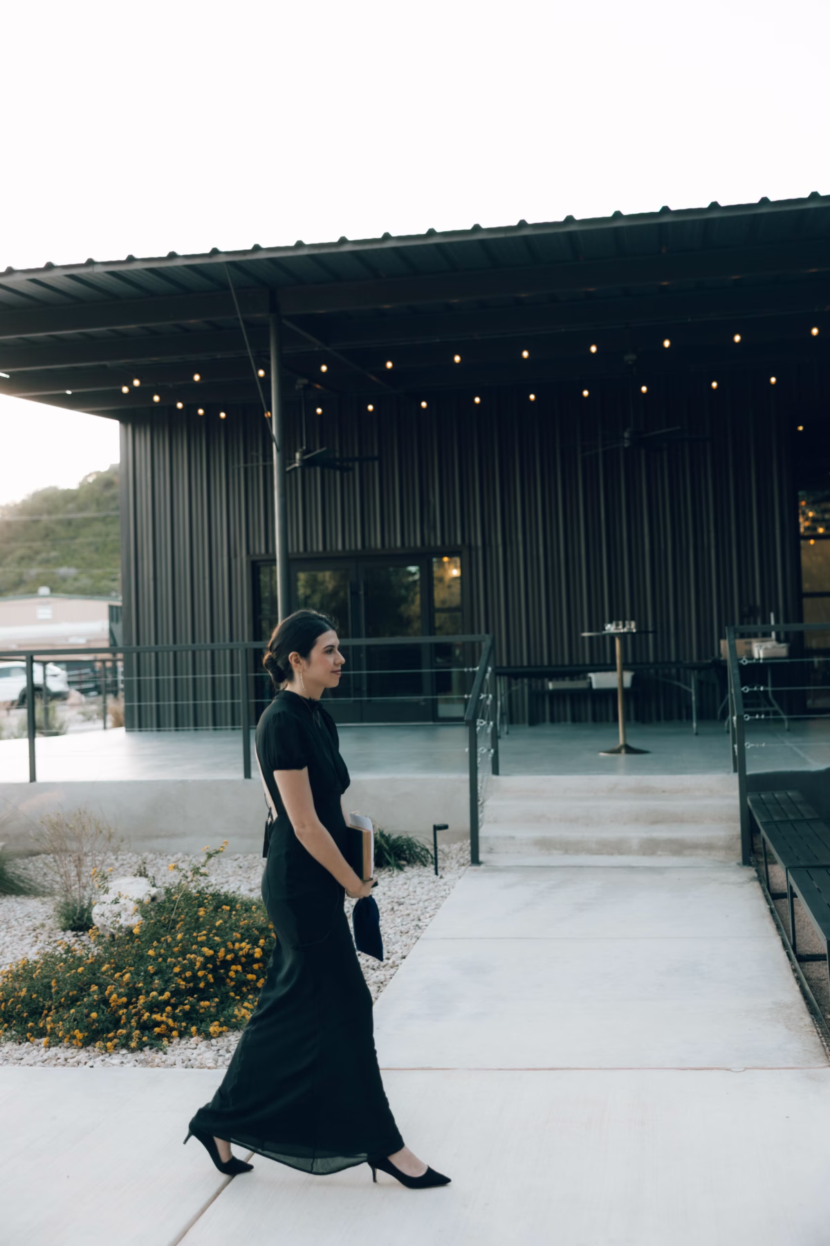 Elegant bride in black dress walking at The Foxwood wedding venue in Hill Country Texas with modern architecture and string lights