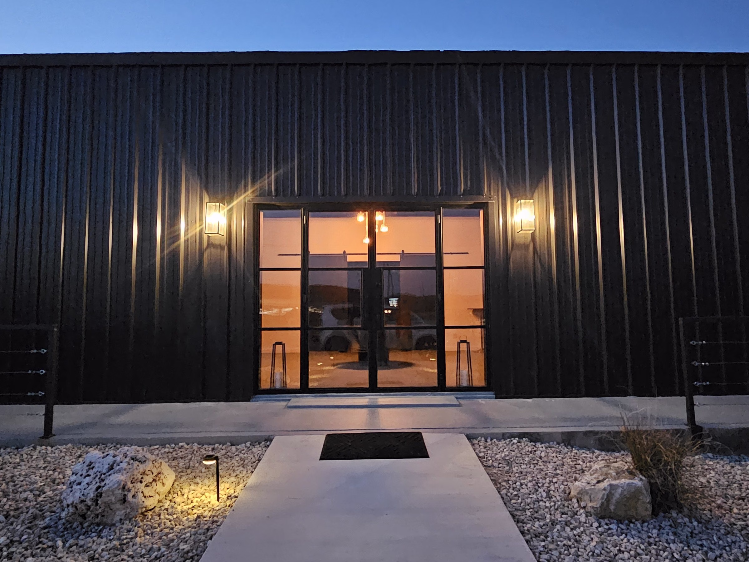 Modern wedding venue entrance at The Foxwood in Hill Country Texas with illuminated glass doors and concrete walkway for private events