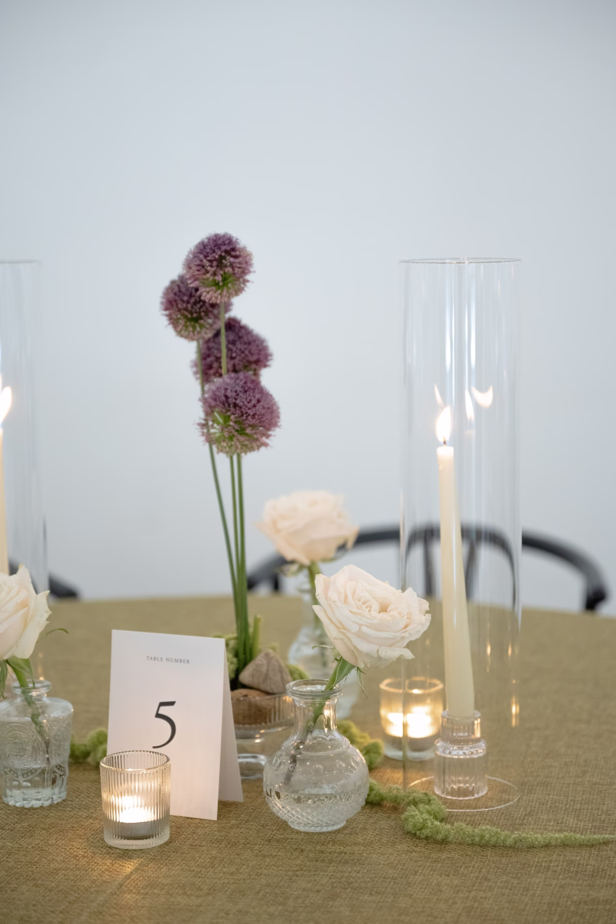 Elegant wedding table centerpiece with purple alliums, cream roses, glass vases and candles at The Foxwood Hill Country Texas venue