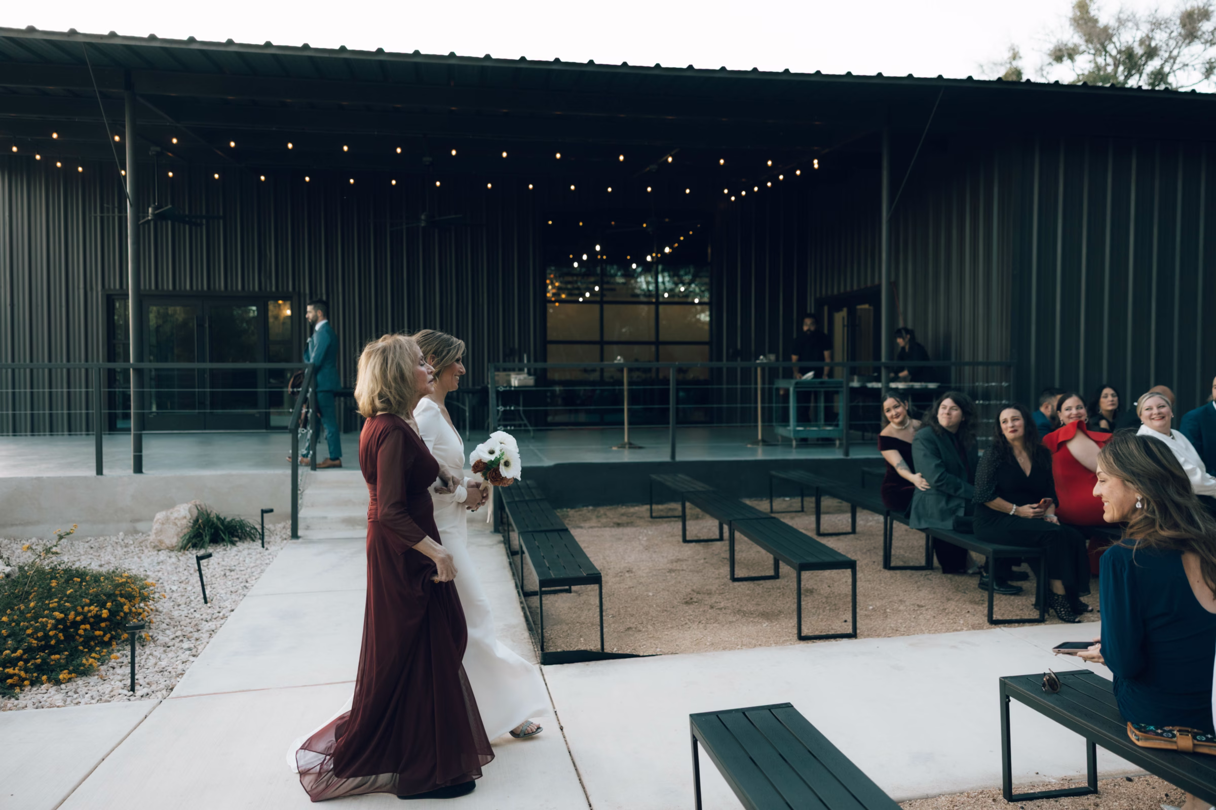 Intimate outdoor wedding ceremony at The Foxwood Hill Country venue with bride in white dress and guests seated on modern benches under string lights