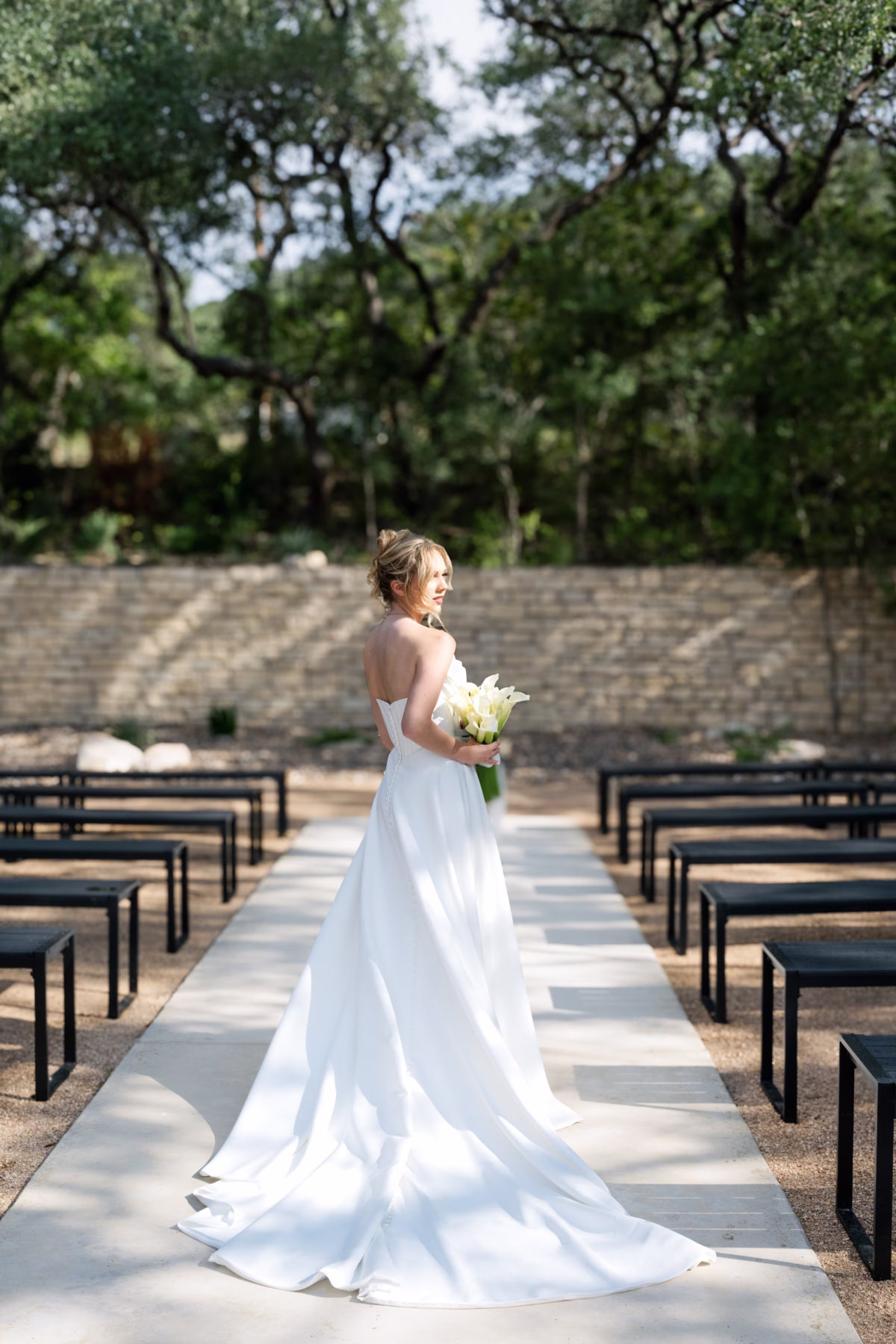 Elegant bride in flowing white gown walking down ceremony aisle at The Foxwood wedding venue in Texas Hill Country