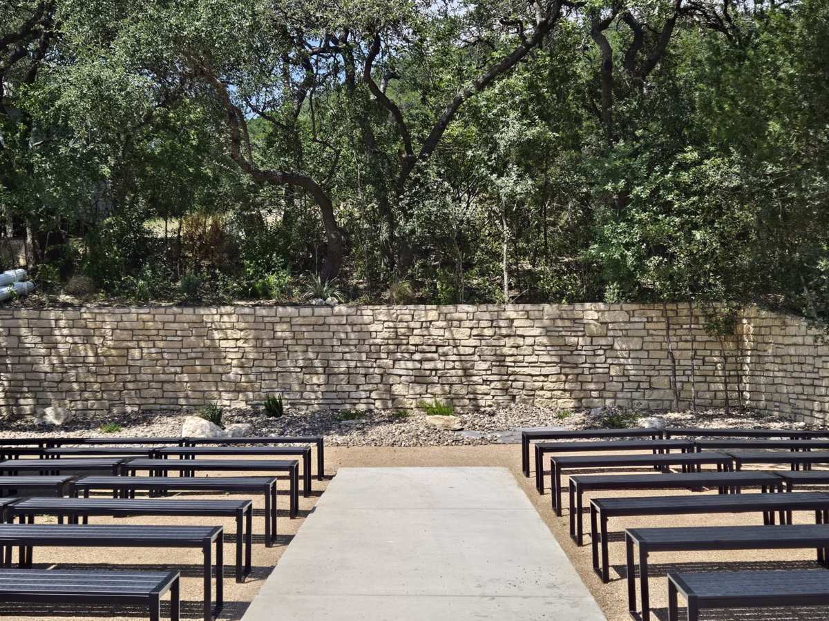 Outdoor wedding ceremony setup with wooden benches and stone wall backdrop at The Foxwood wedding venue in Hill Country Texas