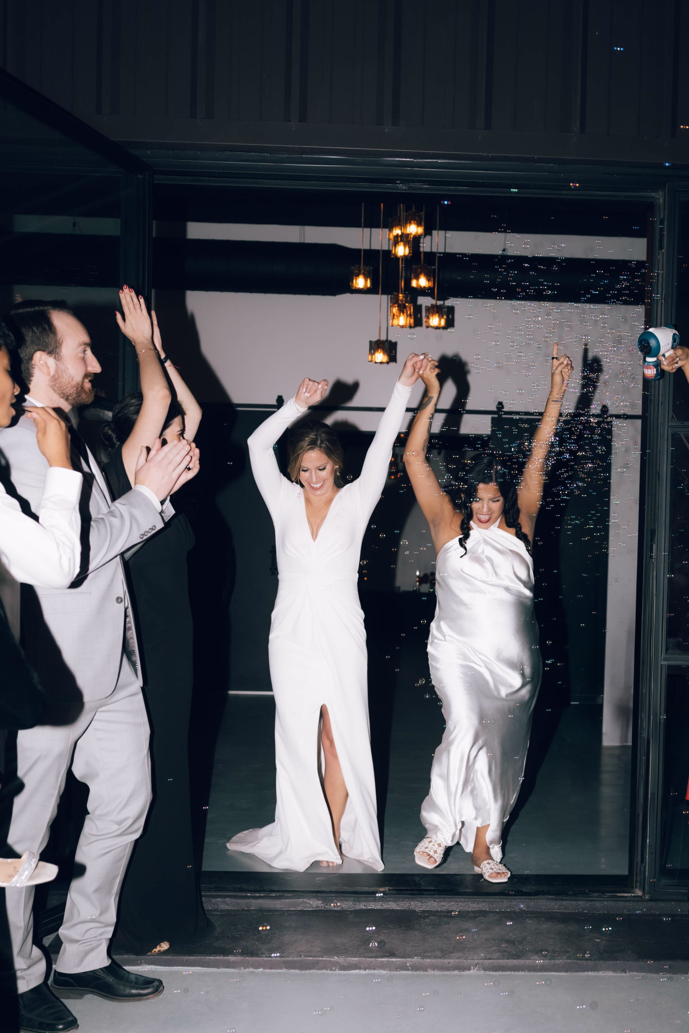 Wedding party celebrating and dancing with arms raised at The Foxwood Hill Country Texas wedding venue with city lights visible through large windows