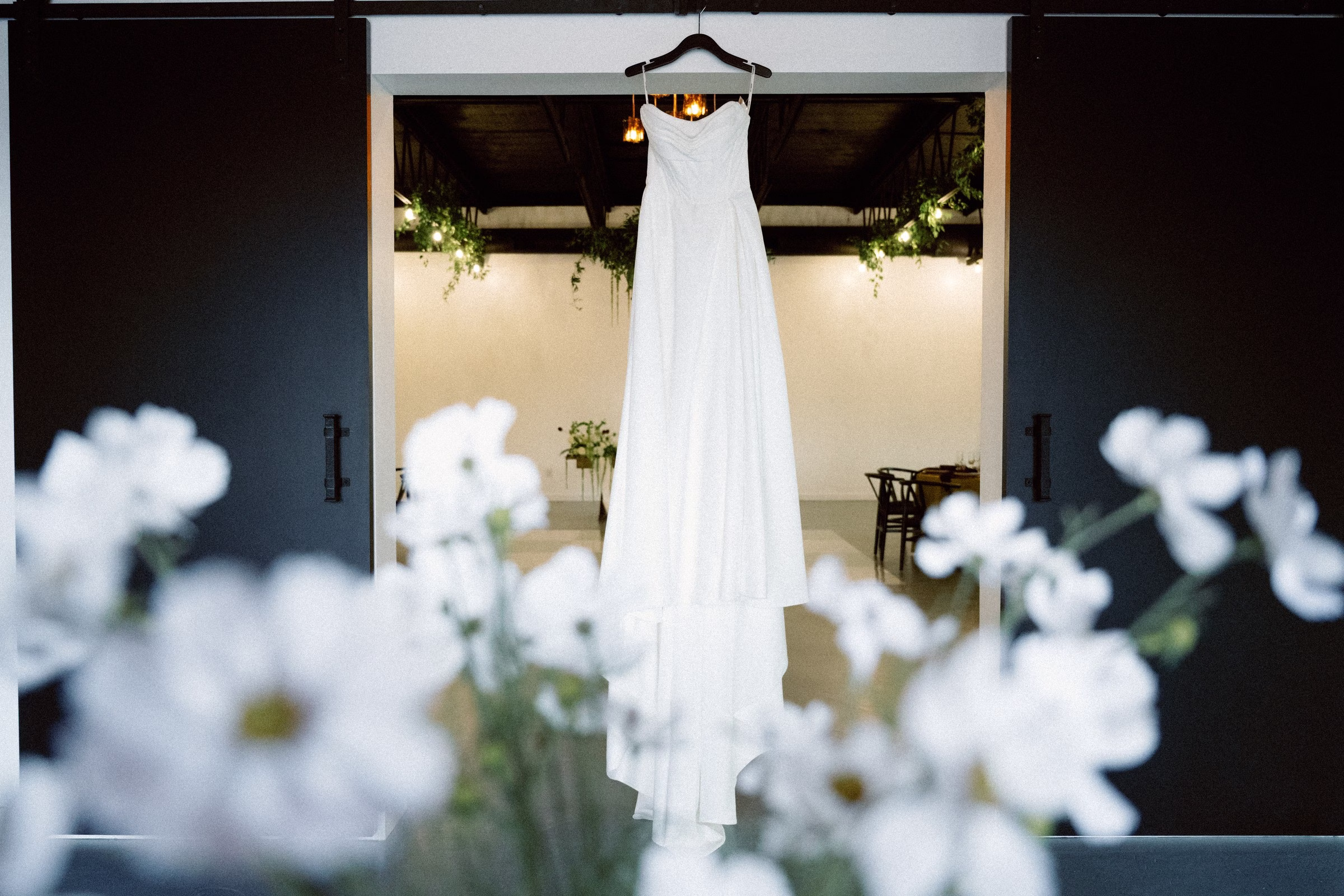 White wedding dress hanging in elegant doorway at The Foxwood Hill Country Texas wedding venue with white flowers in foreground